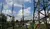 Hochspannungsleitung mit elektrischen Isolatoren und Strommast vor einem blauen Himmel mit Wolken, umgeben von Wohngebäuden und Bäumen.